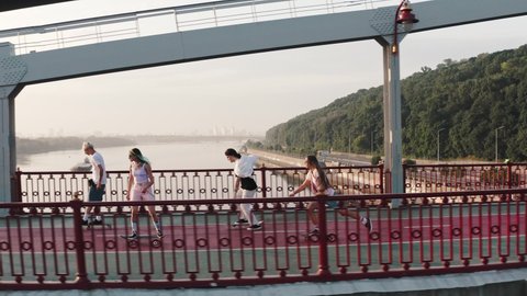 Aerial footage of a group of skaters, boys and girls riding a large bridge across the river at high speed.