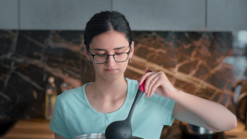 happy girl tasting soup on spoon in modern kitchen and smiling. pretty teen girl prepares soup on the stove in the kitchen. Close-up of a housewife