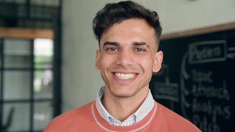Young happy smiling cheerful Indian latin guy Hispanic high school college university student standing in classroom campus laughing looking at camera. Headshot close up portrait.