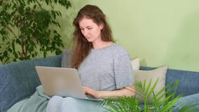 A Woman use laptop on sofa in cozy office. Smile Young student shopping online. video call mom at home in quarantine. notebook look at screen type message. happy lady computer browsing internet media