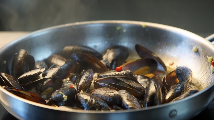Cooking delicious fresh mussels on hot pan in luxury restaurant. Chef shakes and mixes mussels and greens on a grill. Traditional mediterranean cuisine. Slow motion scene. | Shutterstock HD Video #1075732019