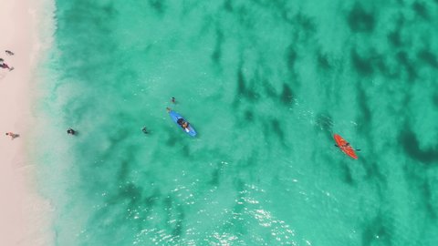 Man in kayak on azure water, sandy beach, aerial view. Clean, transparent water texture near coastal area. People in summer by sea. Amazing nature scenery. Holidays in Indonesia, island Kai Kecil