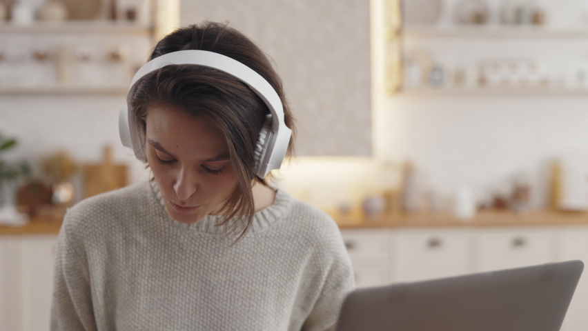 Pretty woman using wireless headphones and laptop for online lesson while staying at home. Female student with short haircut having distance learning during pandemic. Royalty-Free Stock Footage #1075736423