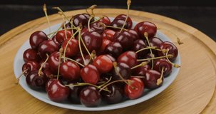 Ripe red cherries on wooden round plate. Fresh appetizing cherries, summer dessert. Rotating turntable clockwise .