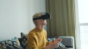 Young boy in a yellow sweater wearing Virtual Reality glasses headset sitting on the sofa playing a videogame.