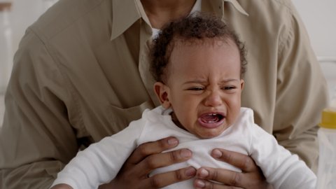 Parenting issues. Close up portrait of upset cute african american baby boy crying in fathers hands, feeling stressed and annoyed, tracking shot, slow motion