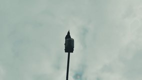 Black crow silhouette sitting on lamppost and croaks. Dark raven sits on street lantern and caw by cloudy sky, bird voice