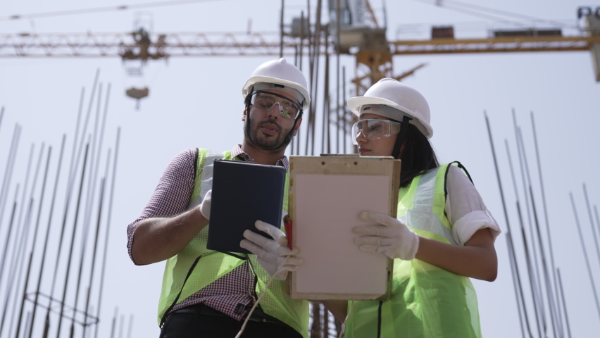 Two Indian engineers lady and man wearing safety helmets and face mask with eyeglass they have a discussing conversation together on construction site.Foreman and his assistant lady talking together. Royalty-Free Stock Footage #1075747553