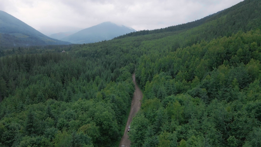 aerial view of suv car moving by path road in mountains overcast misty rainy weather tracking dolly shoot