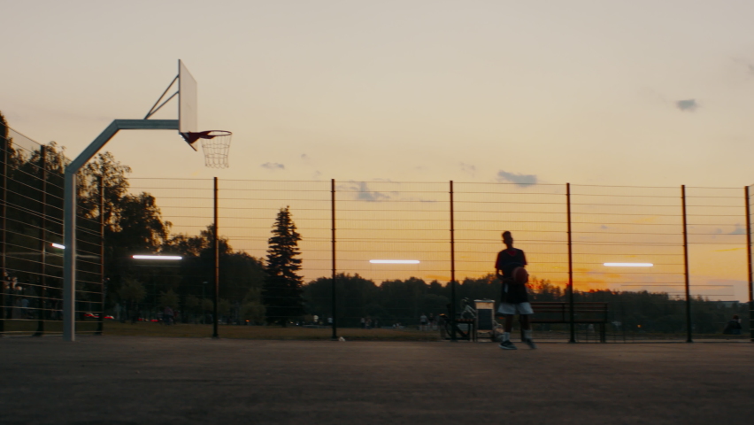 Black African American teenager kid boy playing basketball alone on an outdoor court in the evening. High quality 4k footage Royalty-Free Stock Footage #1075756532