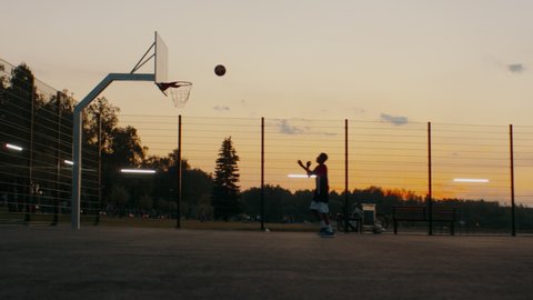 Black African American teenager kid boy playing basketball alone on an outdoor court in the evening. High quality 4k footage