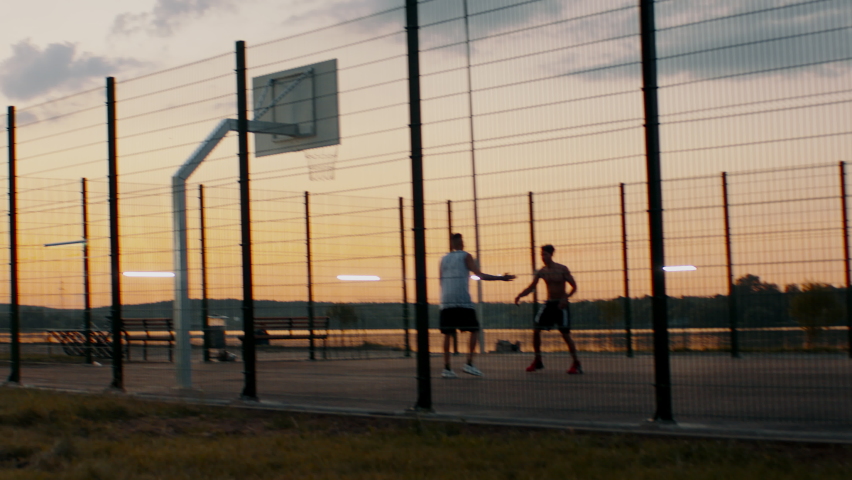 HANDHELD Black African American friends playing 1 on 1 streetball on scenic outdoor court in the evening. High quality 4k footage Royalty-Free Stock Footage #1075756565