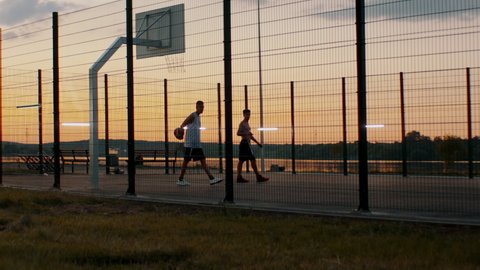 HANDHELD Black African American friends playing 1 on 1 streetball on scenic outdoor court in the evening. High quality 4k footage