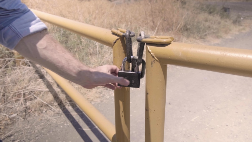 Hands unlocking lock on yellow gate close up. A field in the countryside. cowboy on a farm opening yellow metal gates. letting the cattle out. Hot summertime in the wild west. desert view.
