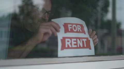 Man placing a FOR RENT sign in the window.
