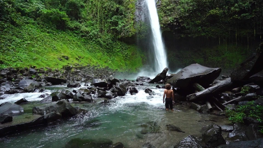 La Fortuna Waterfall, Costa Rica An unidentified boy stands in the water and looks at the waterfall