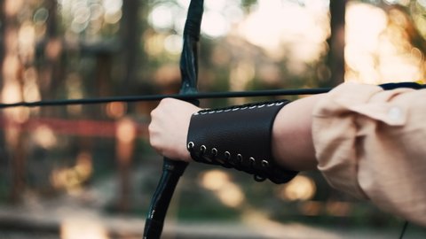 A girl shoots from a bow at targets. Archery sports, outdoor training. Wooden bow and arrow, accuracy, hitting the target. Evening light. Female focusing to the target.