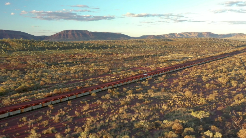 AUSTRALIA - CIRCA 2020s - 2021 - Excellent aerial shot of a coal train traveling past shrubs and mountains in Tom Price, Australia.