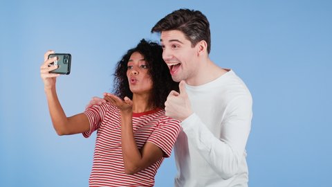 Young interracial couple making selfie with smartphone on blue studio background. African american woman and white man smiling, having fun. Love, holidays, happiness concept.