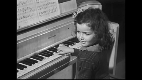 CIRCA 1931 - A little girl thumbs through sheet music and plays the piano without looking at the keys.