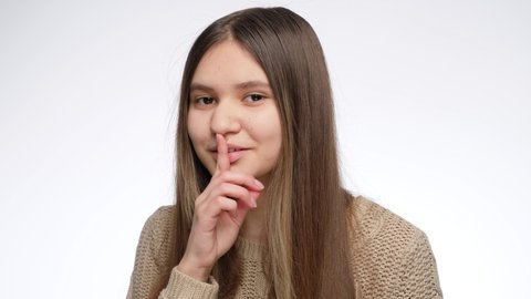 Cute smiling girl holding finger at mouth in shhh gesture after telling secret.