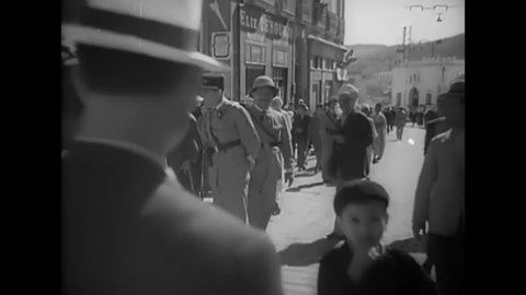 CIRCA 1940s - French soldiers patrol a large group of Arab men walking through an Algerian city.