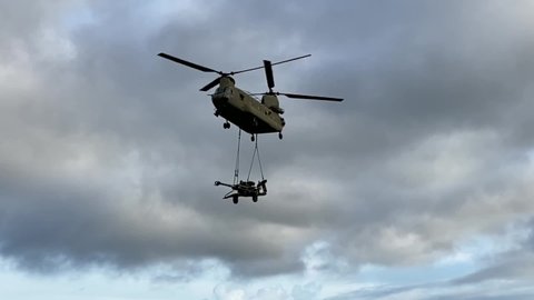 CIRCA 2019 Slow motion, U.S. Army CH-47 Chinook helicopter sling-loads M777 Howitzer during troop support military exercise.