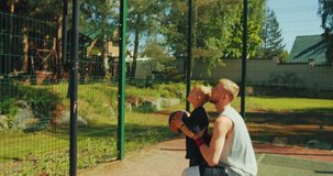Young sportive father with son in hands playing basketball. Kid boy throwing ball in basketball hoop outdoors