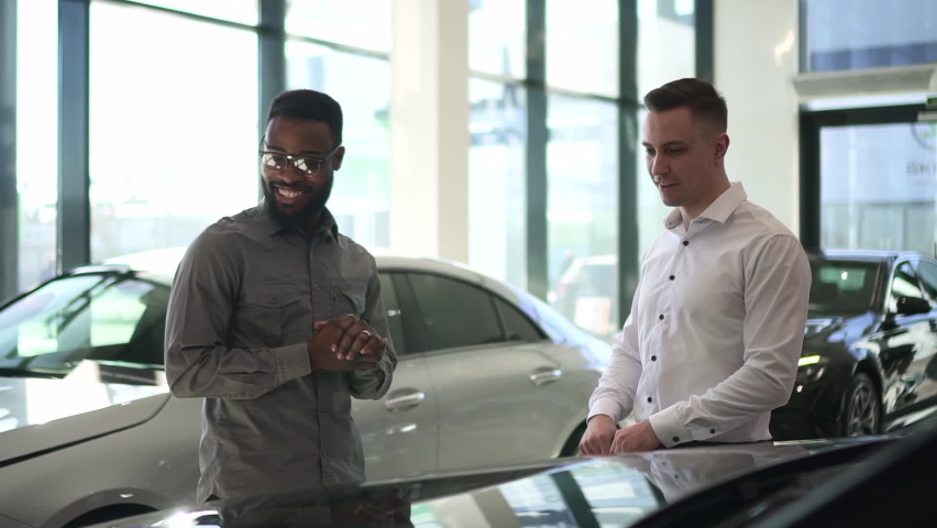Car purchase in dealership salesman shows the car to a black man  Royalty-Free Stock Footage #1075796741