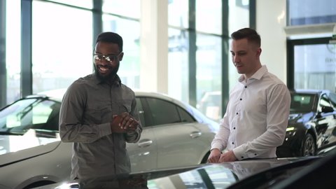 Car purchase in dealership salesman shows the car to a black man 