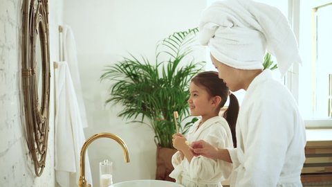 Child and mother brushing teeth, look at mirror in modern white bathroom. Asian parent