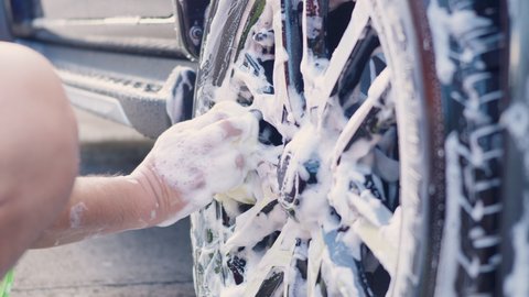 Hand of worker man with foam fabric washing car's alloy wheels on car wash, car care wash clean service concept