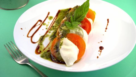 Caprese salad with tomatoes, mozzarella and basil. Red and orange tomatoes with white cheese and sauce. Portion of tomato food on a plate in a restaurant. View from above. Delicious healthy  food.