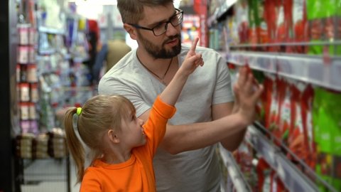 Father and little girl in shopping cart choose products in grocery department in supermarket. People shopping food in store. Grocery store shelves