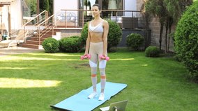 Young beautiful sports girl in leggings and a top does exercises with dumbbells. Healthy lifestyle. A woman goes in for sports outdoor at home.