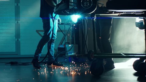 CU Sparks falling on the ground as mechanic welding a go kart car inside garage. 100 FPS slow motion. Shot with 2x anamorphic lens
