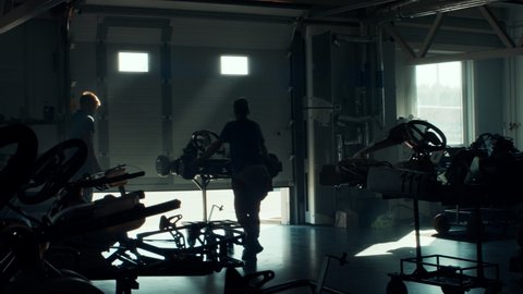 WIDE Trainer opens the door as a teenager kid boy professional racer takes his go kart out of the garage. Shot with 2x anamorphic lens