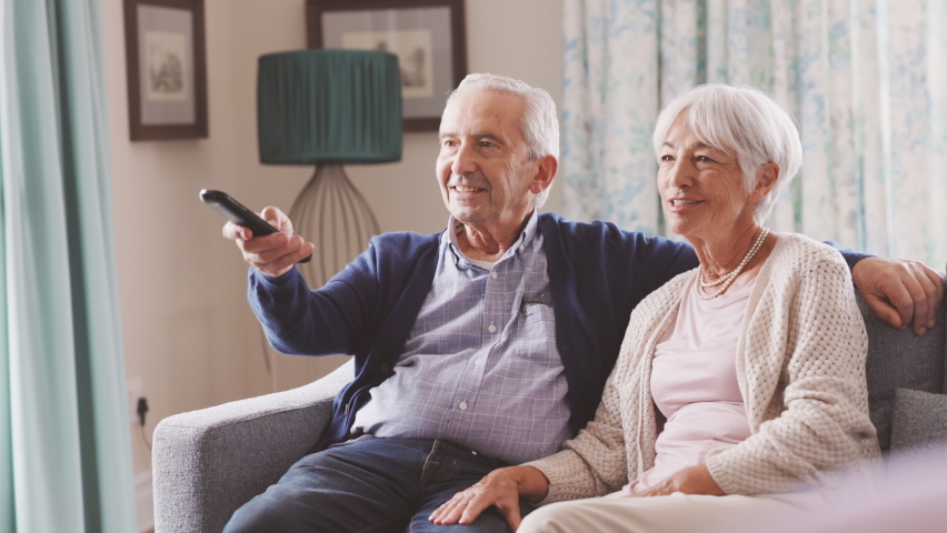 Happy senior couple in living room using remote control to change channel. Seniors watch TV for entertainment while man using remote control. Cheerful wife and old man sitting on couch in living room. Royalty-Free Stock Footage #1075814246