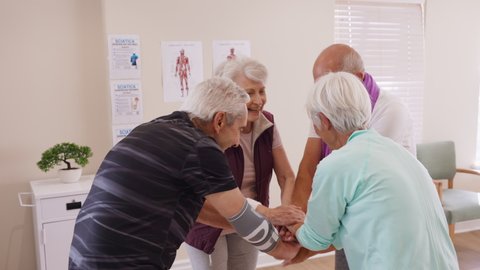 Laughing senior people putting hands together at clinic after workout. Happy group of retired people smiling and stacking hands after exercise session at nursing home. Smiling group of eldelry team.