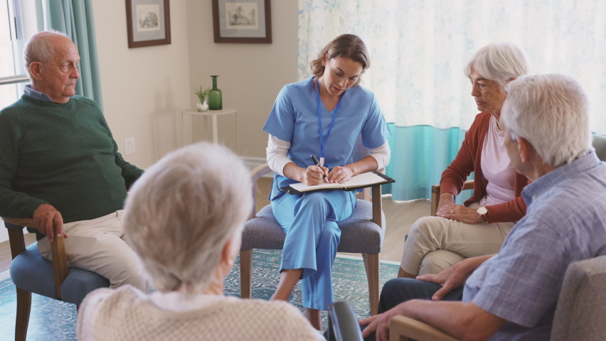 Group of senior people listening to young nurse. Psychological support group for elderly and lonely people in a community centre. Group therapy in session sitting in a circle in a nursing home.