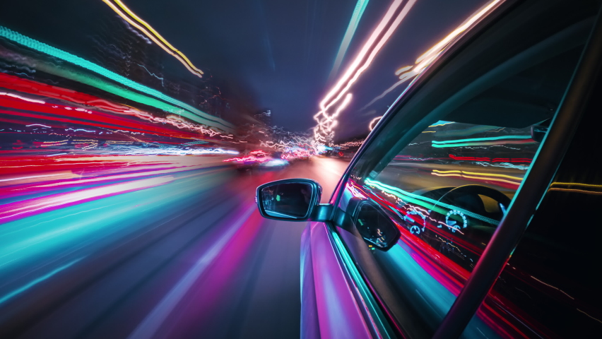 Beautiful motion timelapse of a speedy night drive in a big city, seamlessly looped. Side view from the car window to the road with neon light trails from vehicles and street lights. Royalty-Free Stock Footage #1075818986