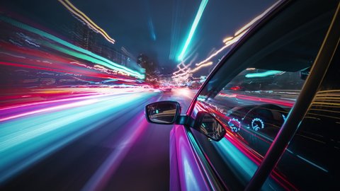 Beautiful motion timelapse of a speedy night drive in a big city, seamlessly looped. Side view from the car window to the road with neon light trails from vehicles and street lights.