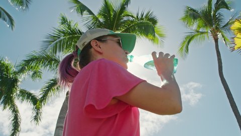 Woman drinks water, relaxing outdoors in tropical park in summer sunny day. Health, wellbeing, wellness, sense of balance and calmness. Workout and fitness training on fresh air with nature views 4K