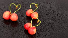 Two cherries with drops tied into a heart love. Sweet cherry love sign on white background. Two heart shaped berries with intertwined stems. 4K UHD video footage 3840X2160.