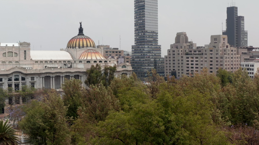 Reveal of city, ascending drone flying around colourful dome with bird sculpture of Palace of fine arts (Palacio de Bellas Artes) in historic city. Mexico City, Mexico.