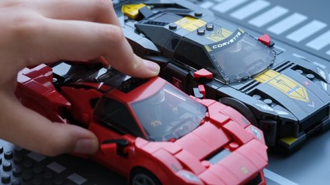 Tambov, Russian Federation - July 07, 2021 A child moving a Lego Ferrari F8 Tributo car to the Lego Chevrolet Corvette C8.R race car that is parked on the road baseplate. Lego Speed Champions.