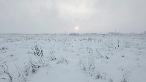 Sunset over a snowy field in nature in winter. The camera is flying low over the ground