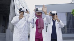 Outdoors shot of multiracial team of three male and female doctors wearing virtual reality glasses, train for better diagnostics, standing in front of modern clinic. Patient examination - Powered by Shutterstock - Get 15% off with code: PIKWIZARD15