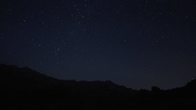 Timelapse of moving star trails in night sky. A view of the stars of the Milky Way with a mountain top in the foreground. Night sky nature summer landscape. Perseid Meteor Shower observation.