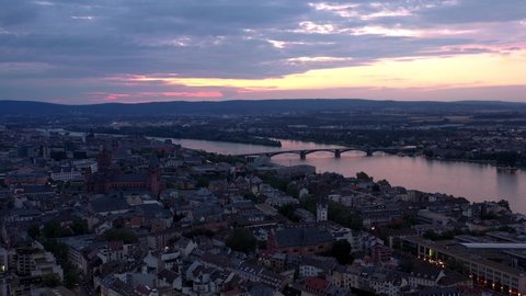 Sideways Drone shot of Mainz at magic hour night circling around city center with with the cathedral and the dark Rhine river water in the background showing a colorful sky
